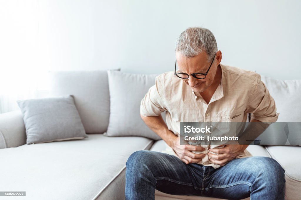 Mature man suffering from stomachache at home Mature man feeling unwell with a stomach ache while sitting at home Stomachache Stock Photo