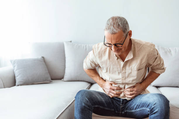 Mature man suffering from stomachache at home Mature man feeling unwell with a stomach ache while sitting at home indigestion stock pictures, royalty-free photos & images