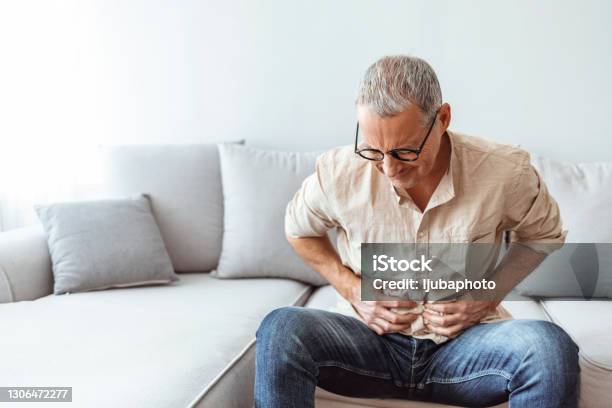 Mature Man Suffering From Stomachache At Home Stock Photo - Download Image Now - Stomachache, Men, Abdomen