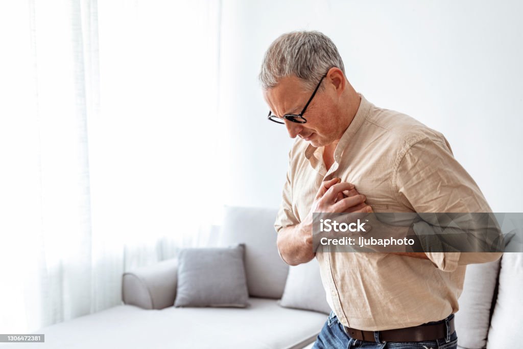 Chest pains are never a good sign Shot of a unrecognizable man holding his chest in discomfort due to pain at home during the day Heartburn Stock Photo