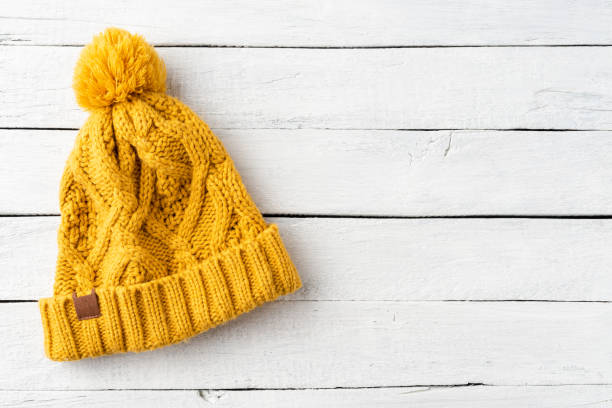 istock Yellow winter hat with pompon on white wooden background with copyspace. Top view 1306477011