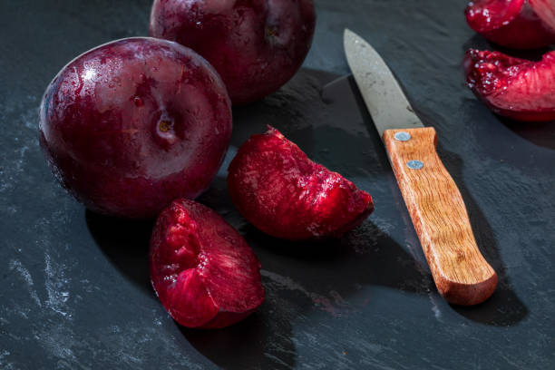 istock Appetizing and healthy red plums, whole and cut into segments with a rustic appearance on a black background. 1306480241