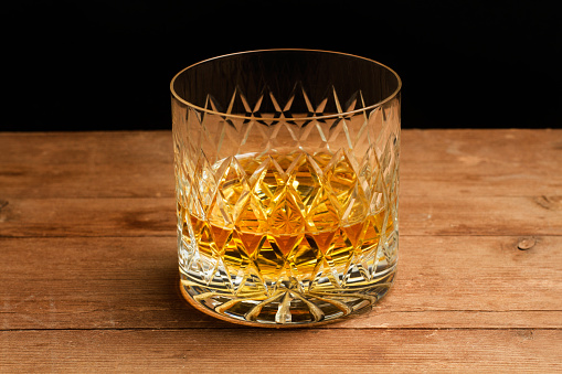 A galss of whisky on a wooden table on a dark background