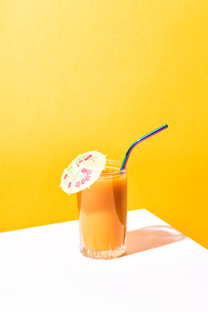 Overhead shot of three cups with cold drinks and colourful straws resting on a wooden table in summer.