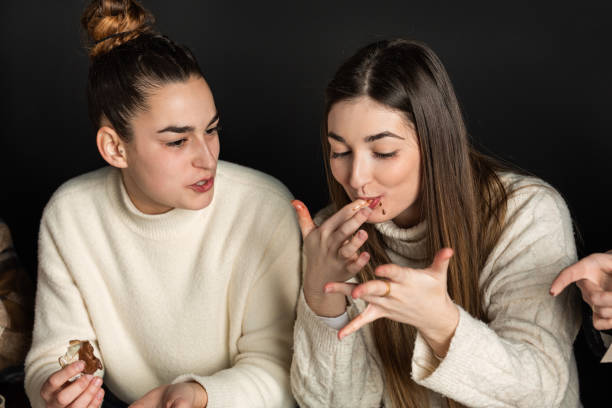 girls lick their fingers while eating chocolate cream desserts cheerful Caucasian girls licking their fingers while eating chocolate cream desserts, wearing casual clothes chocolate fingers stock pictures, royalty-free photos & images