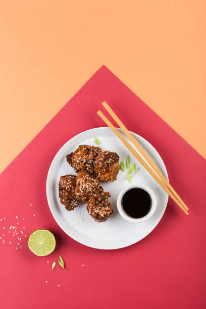 istock Fried chicken teriyaki with sesame seeds on a flat plate with lime, soy sauce and chopsticks on a bright colorful background. 1306486068