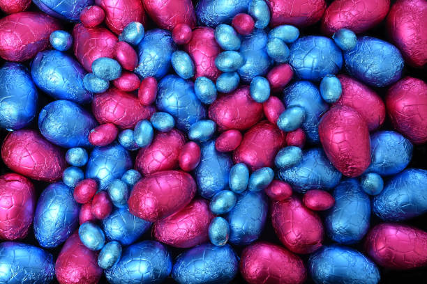 Pile or group of multi colored and different sizes of colourful foil wrapped chocolate easter eggs in blue and pink.