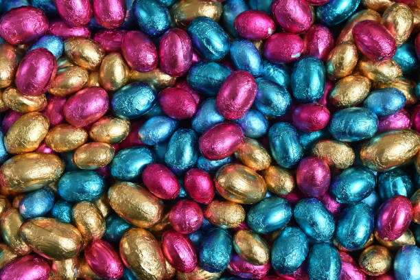 istock Large & small pink, blue and gold foil wrapped chocolate easter eggs, against a peach orange background. 1306491106