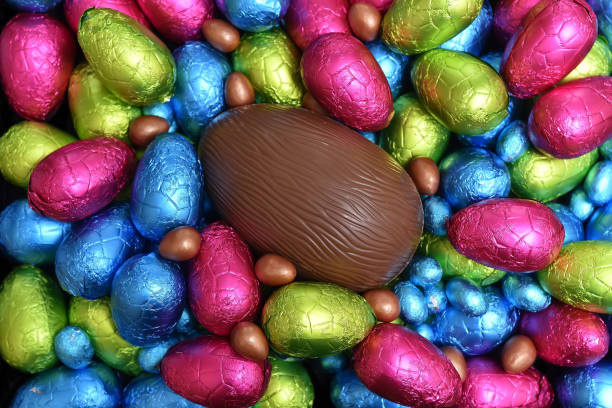 istock Pile or group of multi colored and different sizes of colourful foil wrapped chocolate easter eggs in blue, pink, red, yellow and lime green with a large brown milk chocolate egg in the middle. 1306491109