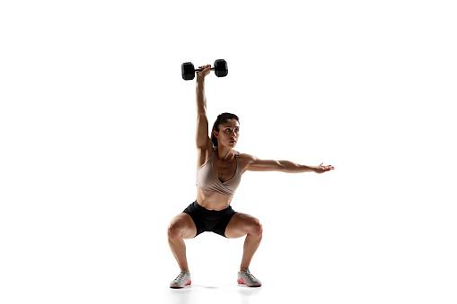 Squats with weight. Caucasian professional female athlete training isolated on white studio background. Muscular, sportive woman. Concept of action, motion, youth, healthy lifestyle. Copyspace for ad.