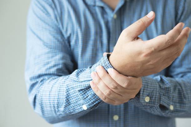 Closeup of male arms holding his painful wrist caused by prolonged work on the computer, laptop. Carpal tunnel syndrome, arthritis, neurological disease concept. Numbness of the hand stock photo