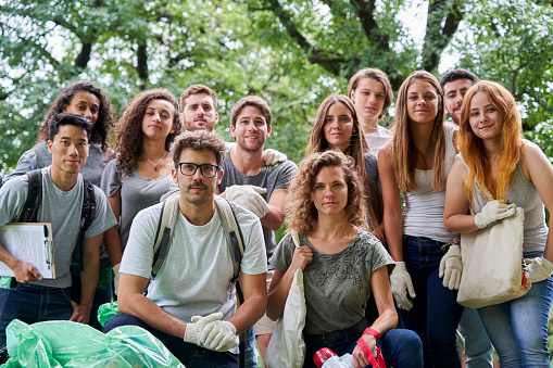 Portrait of a group of volunteers standing together wearing gloves behind garbage bags during daytime