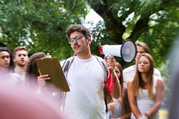 istock Male volunteer looking at clipboard while talking on megaphone in park 1306495194