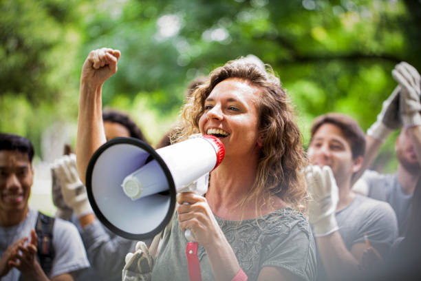 jovem ativista segurando megafone e fazendo um discurso com o punho para cima durante evento de limpeza de lixo - ativista - fotografias e filmes do acervo