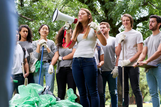 istock Young female volunteer talking on megaphone while standing with her friends in park 1306495592