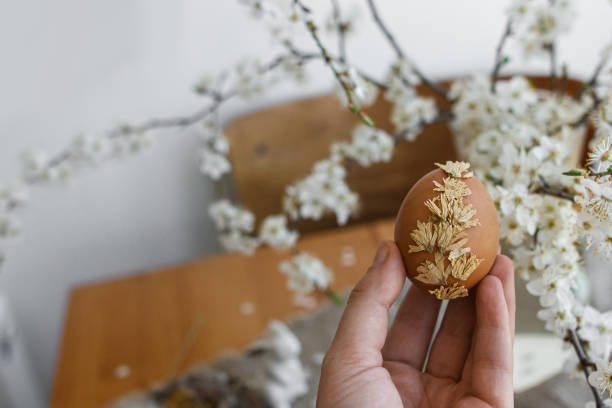 istock Hand holding Easter egg decorated with dry flower at rustic table with linen napkin, cherry blossom 1306495732