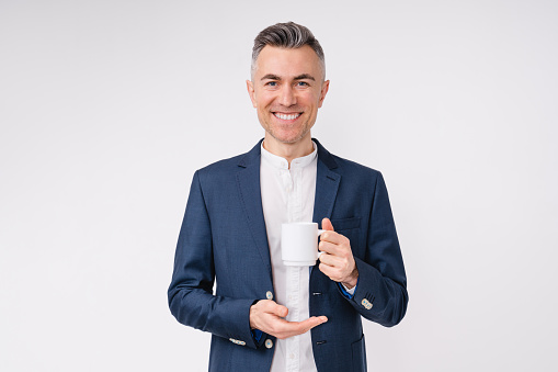 Cheerful mature caucasian businessman holding a cup of hot drink isolated over white background