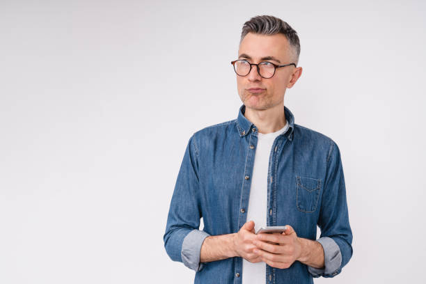 istock Pensive middle-aged man in casual clothes using smart phone isolated over white background 1306498905