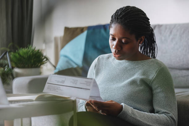 women in business: a young businesswoman reading a utility bill while working from home - pen color image black book imagens e fotografias de stock