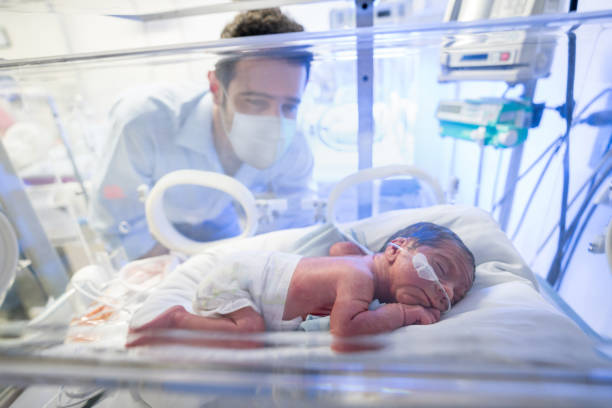 kärleksfull far tittar på sin för tidigt nyfödda i en inkubator medan han bär en ansiktsmask - kuvös bildbanksfoton och bilder