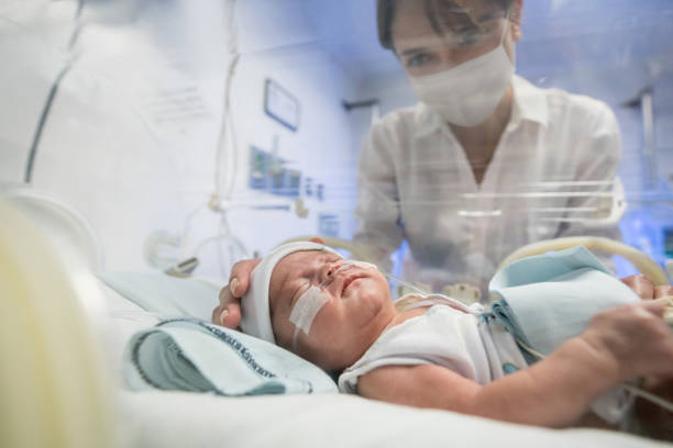 madre amorevole che guarda il suo neonato in un'incubatrice mentre indossa una maschera facciale - premature foto e immagini stock