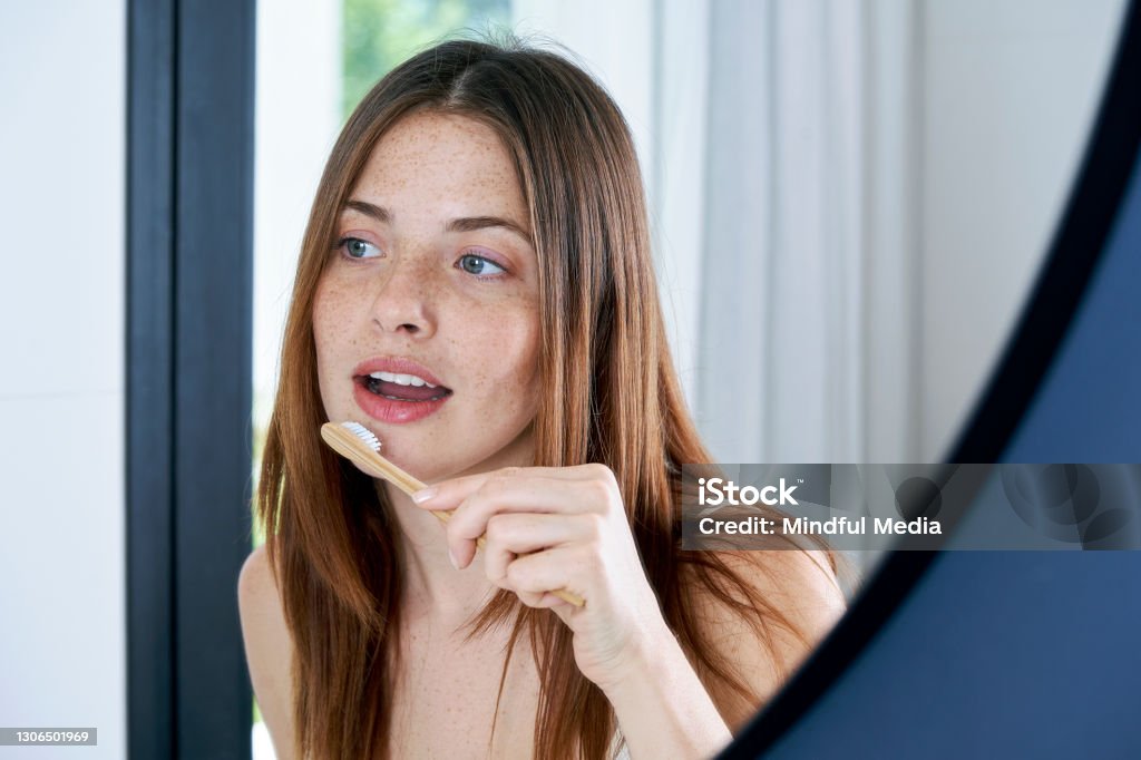 Close up of young woman brushing her teeth at home Smiling beautiful young woman brushing her teeth in bathroom Toothbrush Stock Photo