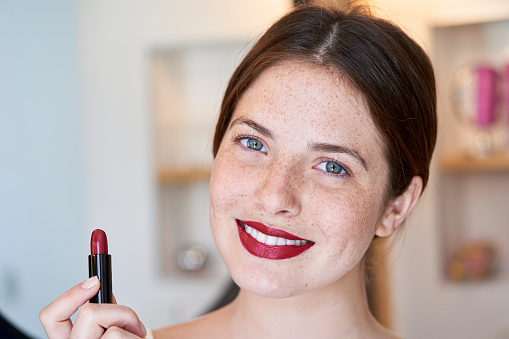 Young woman looking at camera holding lipstick bar