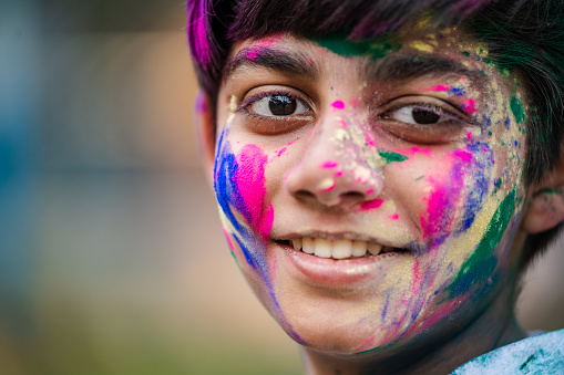 Young boy plays with Holi festival colours. Concepts for Indian festival Holi with Indian boy in outdoor location. Holi is a religious festival in India, celebrated, with the color powders, during the spring.