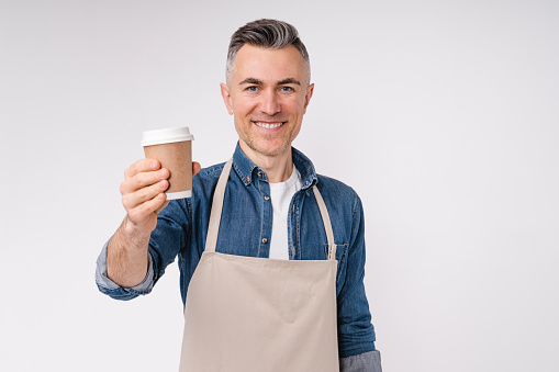 Cheerful white middle-aged barista handing a cup of hot coffee isolated over white background