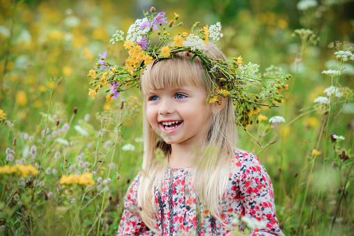 Cute smiling little girl with flower wreath on the summer meadow. Portrait of adorable small kid outdoors