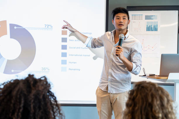 istock Smiling young businessman pointing at projection screen while giving presentation to colleagues in board room 1306509018