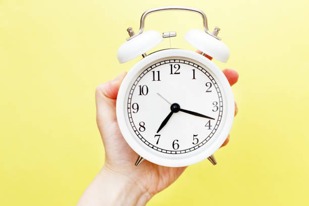 istock female holding white alarm clock in her hand on yellow background 1306510118