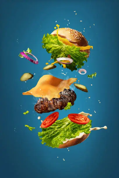 Photo of Hamburger with flying ingredients on blue studio background. Fast food, cuisine concept.