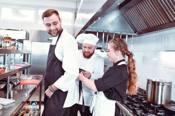 istock Female Waitress And Chef Helping New Cook With Apron 1306512187