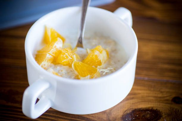 cooked boiled sweet oatmeal with oranges in a bowl on a wooden table