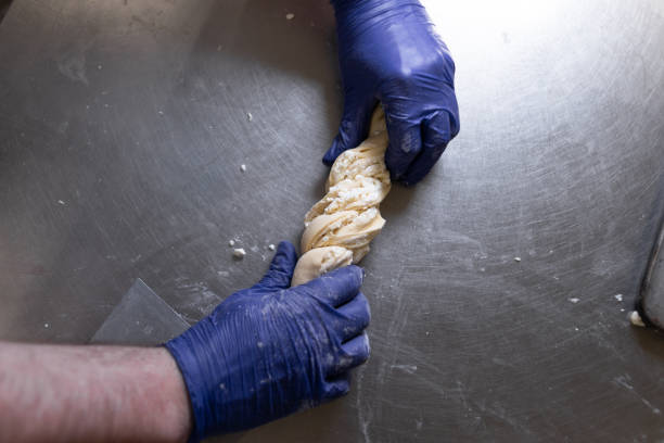 파란색 보호 장갑을 낀 요리사의 손은 코티지 치즈와 설탕으로 채워진 롤을 준비하고 있습니다. 밀가루 제품의 수동 생산. - twisted cheese biscuit pastry 뉴스 사진 이미지