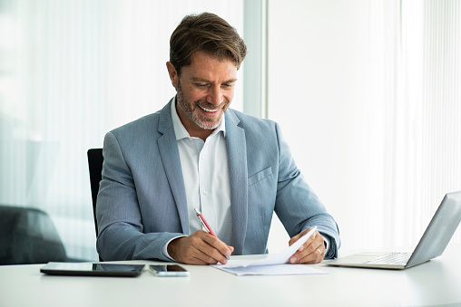 Smiling businessman signing document while sitting in board room