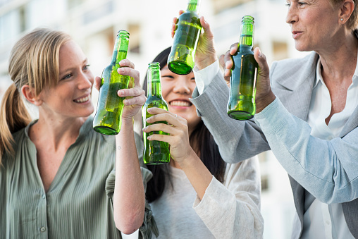Smiling work colleagues toasting beer bottles while standing outdoors