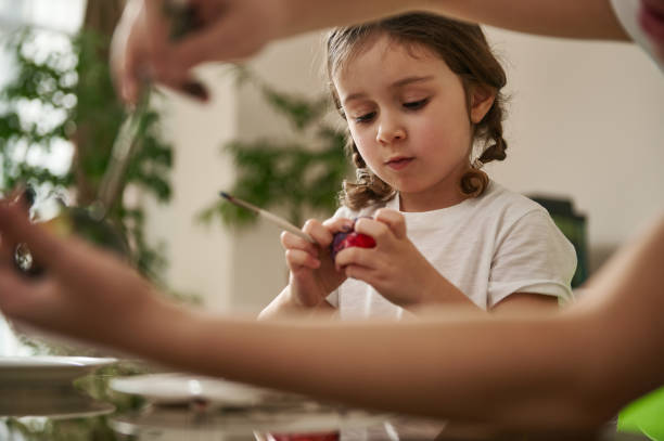 istock View through boy's hands to an adorable little girl decorating an Easter egg 1306517089