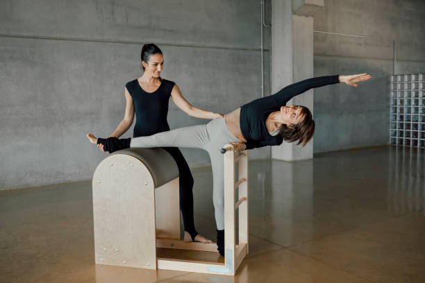 Young woman exercising on a pilates ladder barrel with personal instructor.