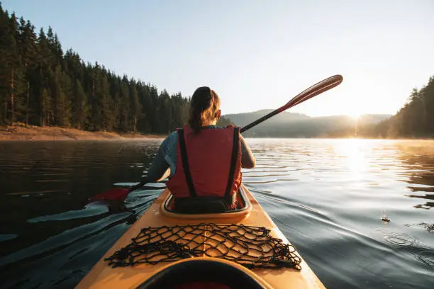 A rear view of a woman kayaking and exploring mountain lake.