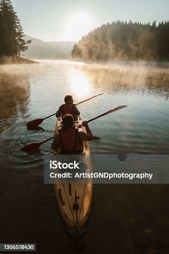 istock Young couple paddling kayak across the mountain lake. 1306518430