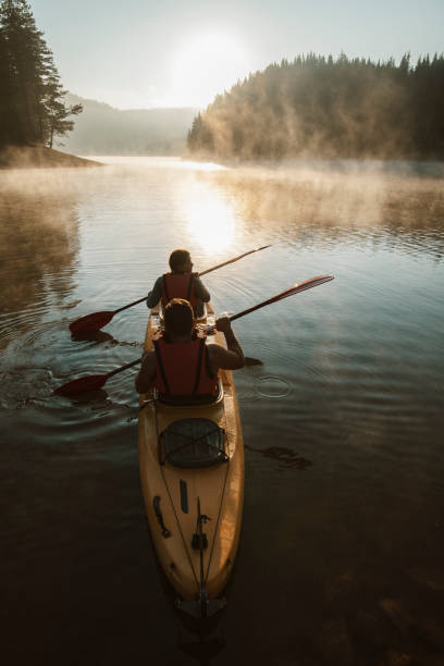 Young couple paddling kayak across the mountain lake. Rear view of young couple exploring mountain lake with kayak. kayaking stock pictures, royalty-free photos & images