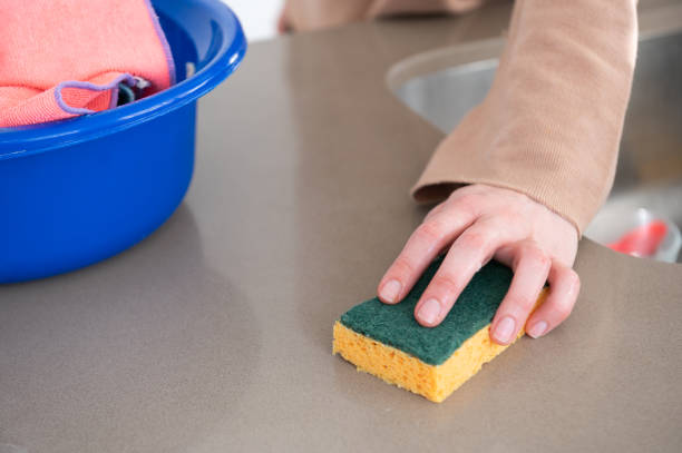 feche acima das mãos da mulher limpando bancada da cozinha com uma almofada de limpeza. nas proximidades eles têm balde com trapos - cleaning domestic kitchen counter top housework - fotografias e filmes do acervo