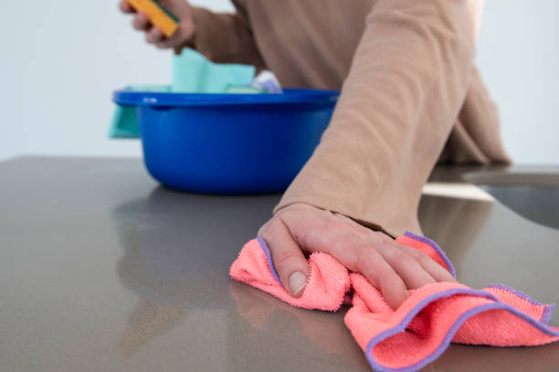 mão da mulher usando um pano colorido para limpar um balcão de cozinha.balde azul com panos de limpeza em um fundo desfocado. - cleaning domestic kitchen counter top housework - fotografias e filmes do acervo