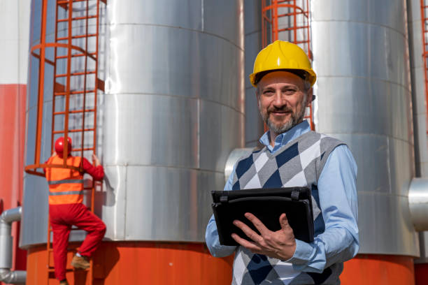 istock Manager or Engineer With Digital Tablet Standing in front of Oil Refinery Storage Tanks 1306520948