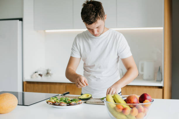 istock Young man making toasts with avocado, tomato, arugula, cheese in modern kitchen. Home cooking 1306530790