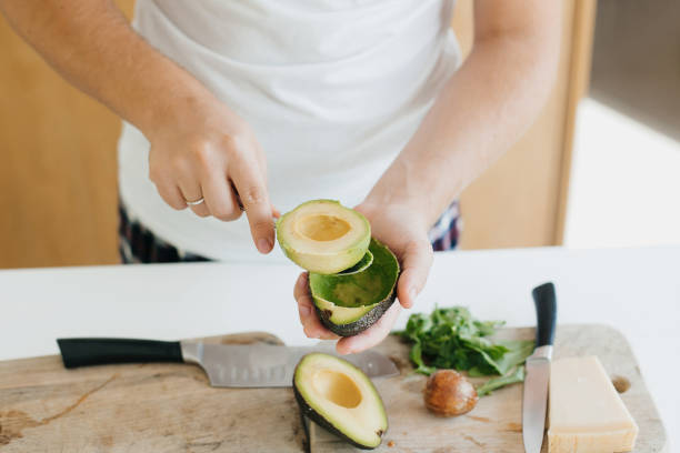 istock Young man peeling avocado and making toasts in modern kitchen. Perfectly ripe avocado in hands 1306530809