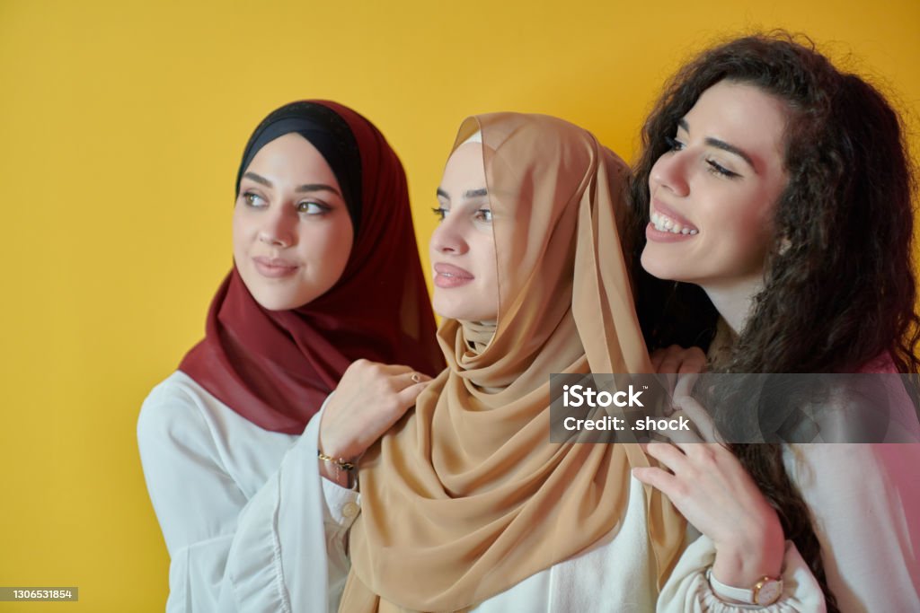 Young muslim women posing on yellow background Young muslim women posing on yellow background. Happy and pretty girls two wearing hijab representing Ramadan concept Women Stock Photo