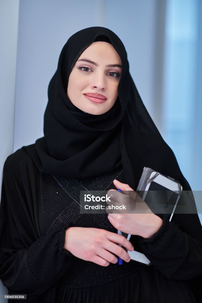 Young Arab businesswoman in traditional clothes or abaya with tablet computer Young Arab businesswoman in traditional clothes or abaya with tablet computer in front of black chalkboard representing modern islam fashion technology Abaya - Clothing Stock Photo